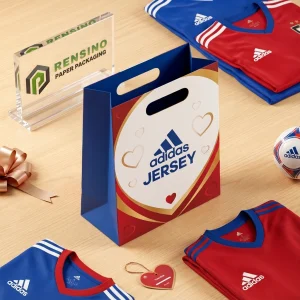 Sac en papier cadeau bleu et rouge avec design de maillot Adidas imprimé et motif de cœur, adapté pour les cadeaux, le commerce de détail ou l'emballage promotionnel, service OEM/ODM disponible
