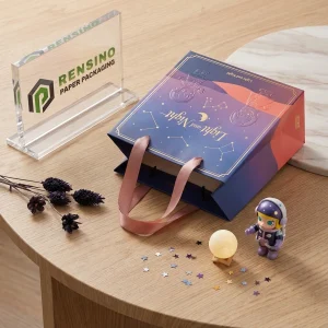 Sac en papier bleu et violet avec un motif d'astronaute et de constellation, adapté pour l'emballage cadeau, impression de logo personnalisée disponible