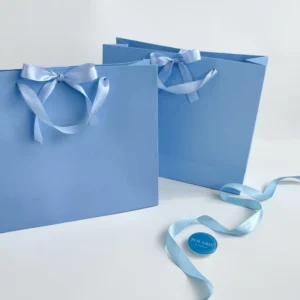 Durable Baby Blue Paperboard Gift Bags with Satin Bow Ribbon Handles and Matte Lamination for Cosmetics